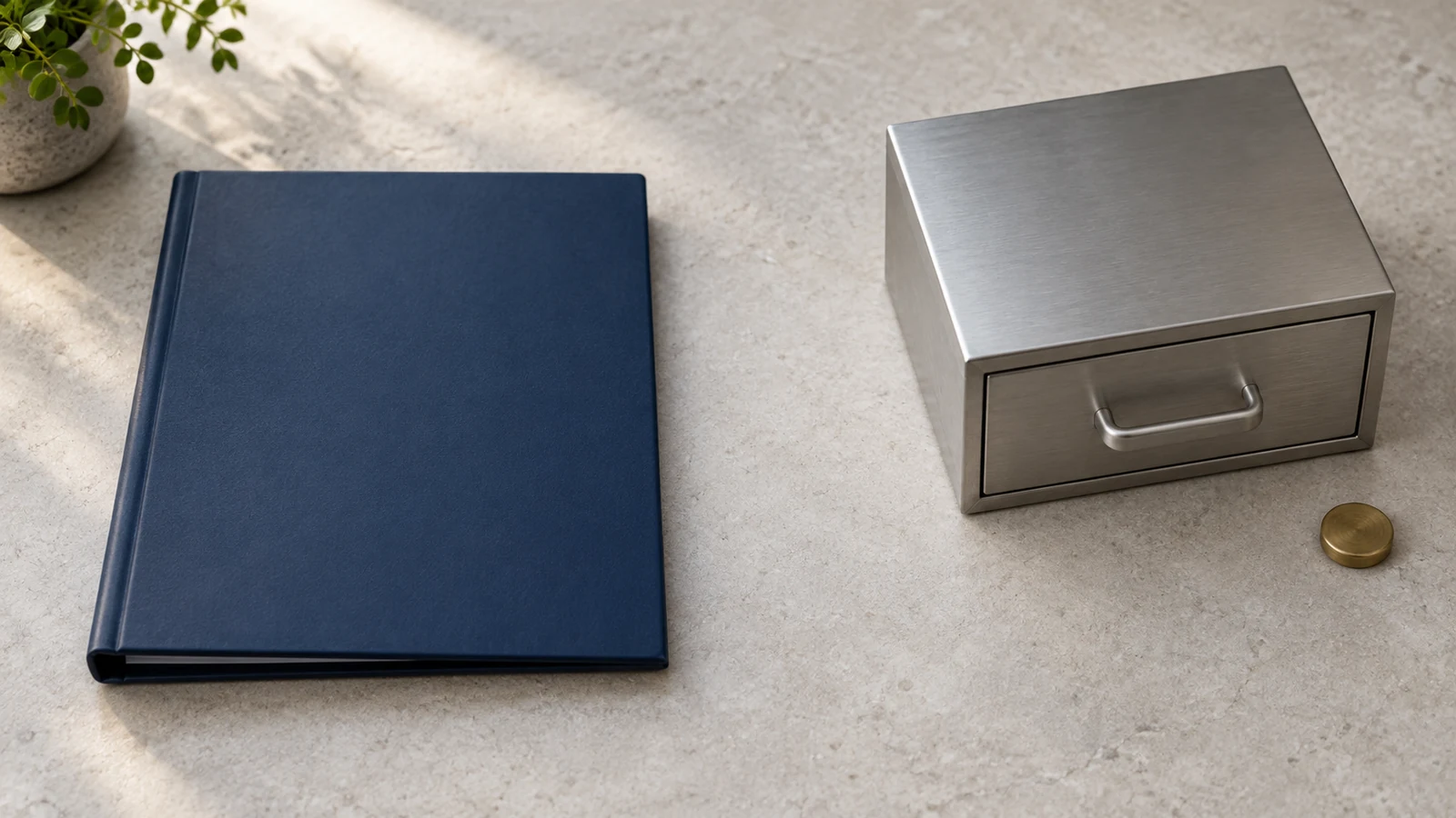 Neutral editorial still life on a pale stone work surface showing an unbranded deep navy document binder on the left, representing the written plan document that governs a one-participant 401(k), and a closed brushed-steel institutional storage drawer on the right, representing third-party custody. A single small unmarked brass disc rests beside the steel drawer. A clear gap separates the document from the custody compartment, and no people, company names, logos, readable text, figures or dates appear.